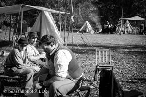Black and white image of historical reenactors gathered at a traditional camp setting.
