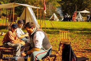 Historical reenactment camp with white canvas tents and autumn foliage in background.