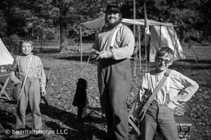 Civil War reenactors in period clothing gather around a campsite with white tents in autumn.