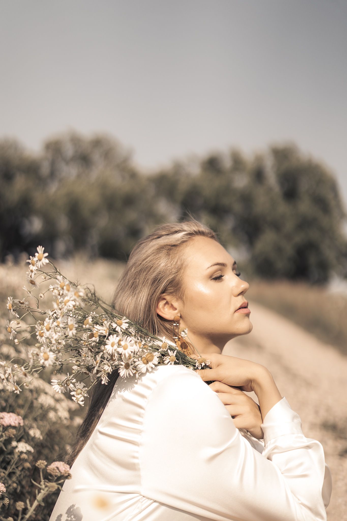 A person in a white sweater poses dreamily in a field of delicate white flowers.