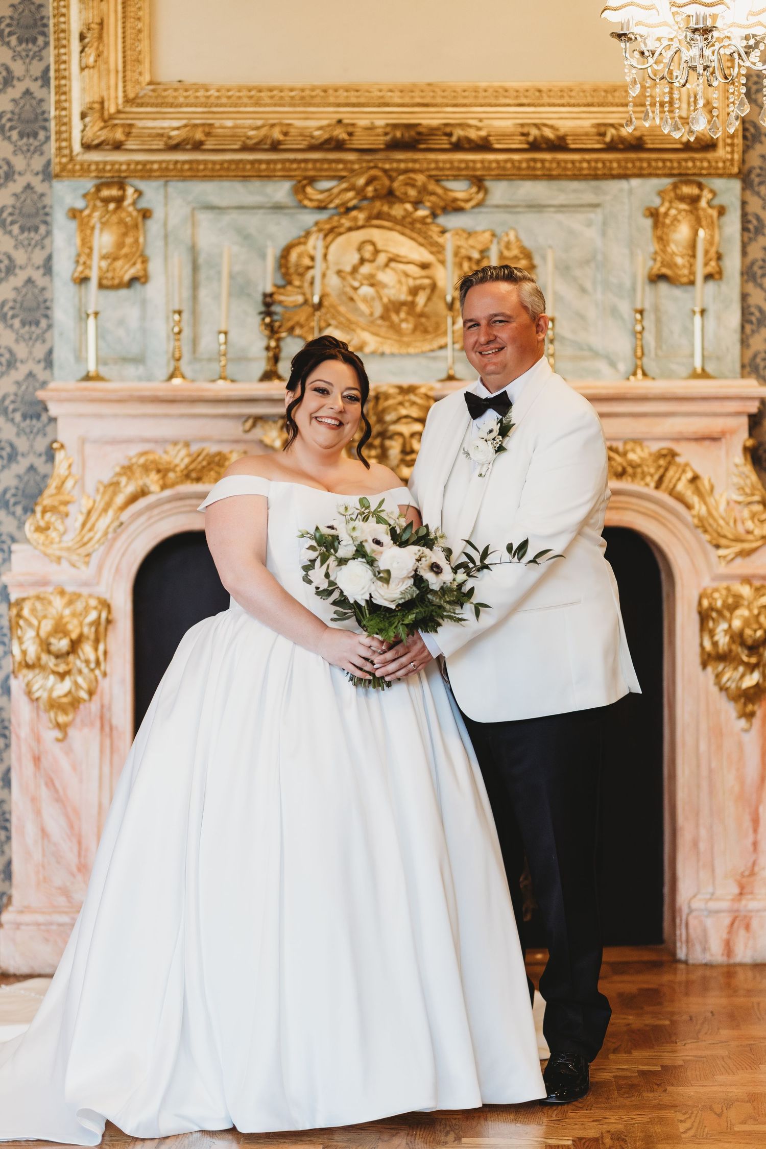 Wedding couple in elegant white attire shares romantic moments in an ornate ballroom with gilded decor and chandeliers.
