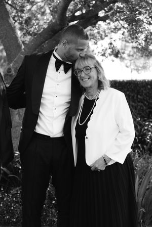 A couple in formal black and white attire share an intimate moment while standing together outdoors.