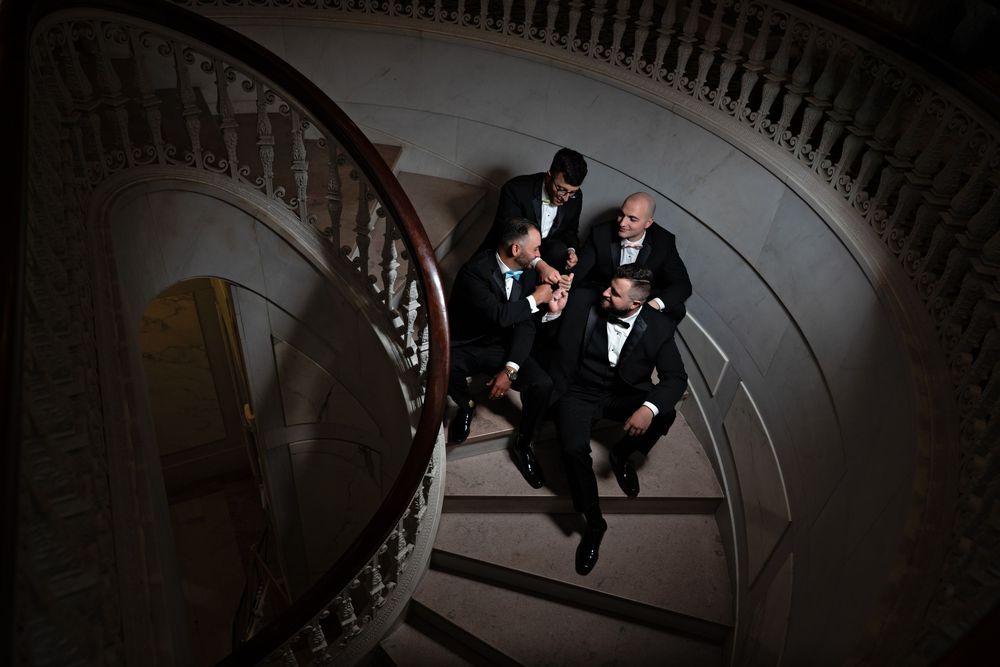 A bride and groom walk down an elegant spiral staircase with ornate railings in a dramatic black and white photo.