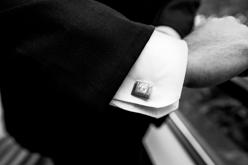 A close-up view of hands adjusting a white shirt cuff with cufflinks.