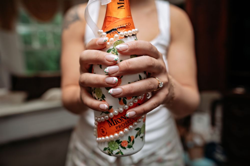 A close-up shot of hands holding a glass of iced beverage with orange and mint garnish.