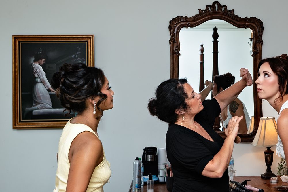 People getting ready for a special occasion with makeup and styling in a room with a framed portrait on the wall.