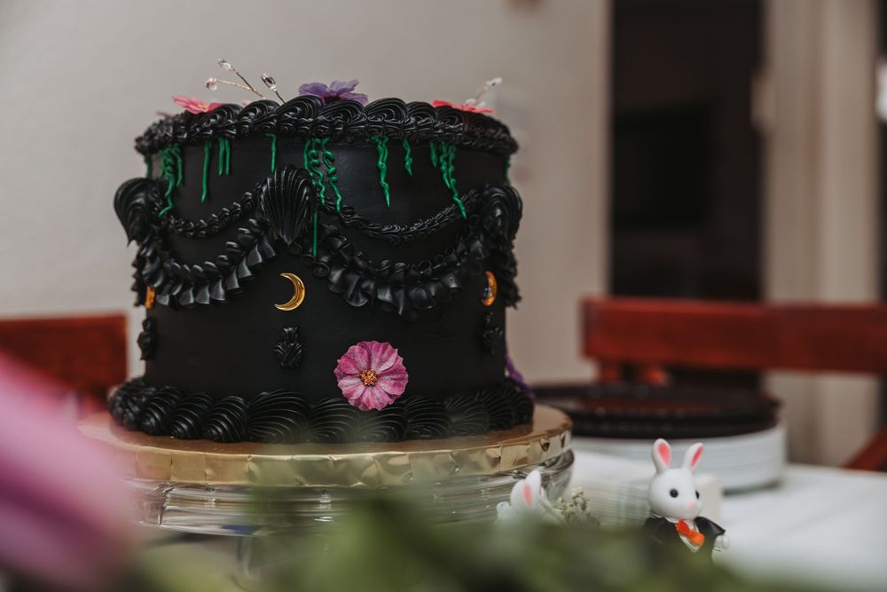 A black frosted cake decorated with colorful flowers and golden accents sits on a display stand.