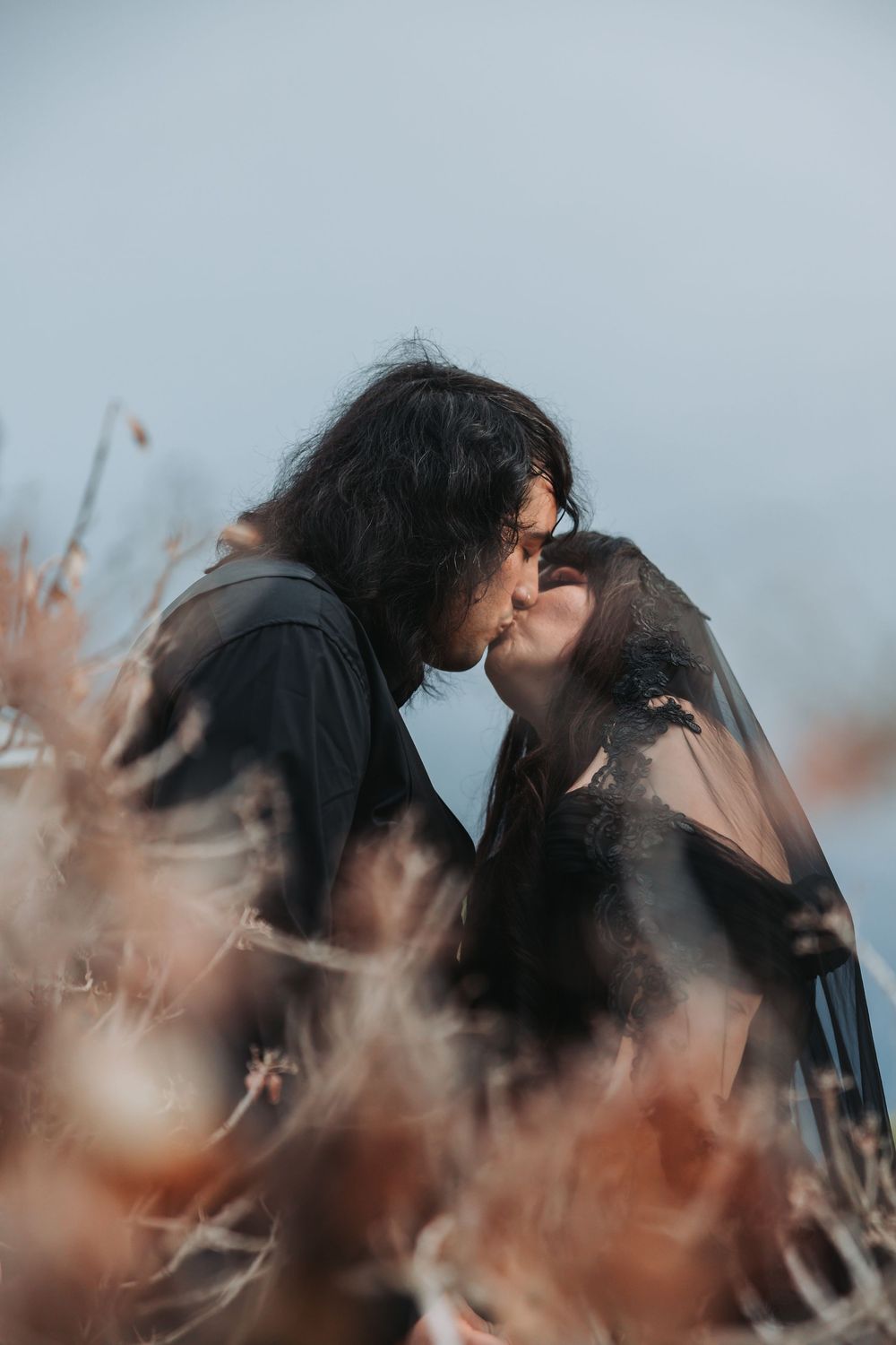 Silhouettes in a tender moment among dried autumn flowers and branches against a misty backdrop.