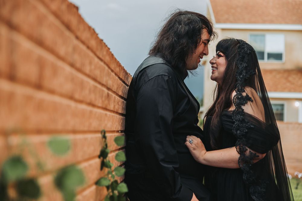A couple embraces intimately against a brick wall in a romantic outdoor setting.