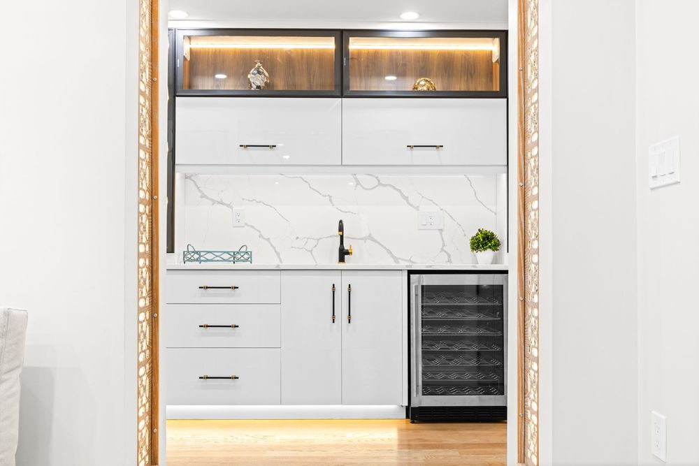 Elegant wet bar with white cabinets, marble backsplash, wine fridge, and wood upper cabinets with LED lighting.