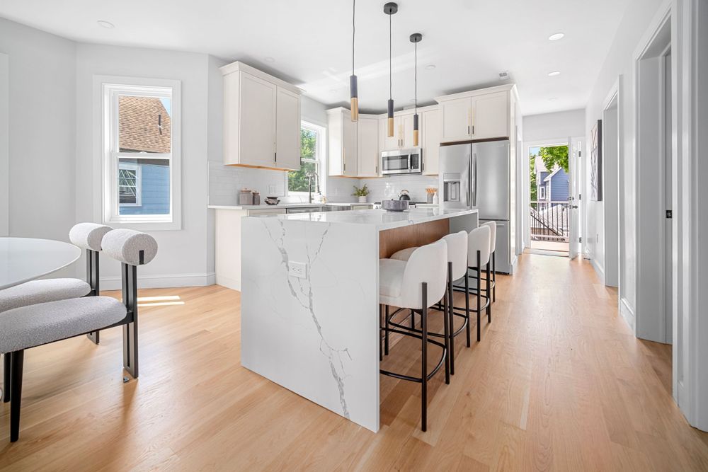 Modern kitchen with marble waterfall island, bar seating, white cabinets, and light hardwood floors.