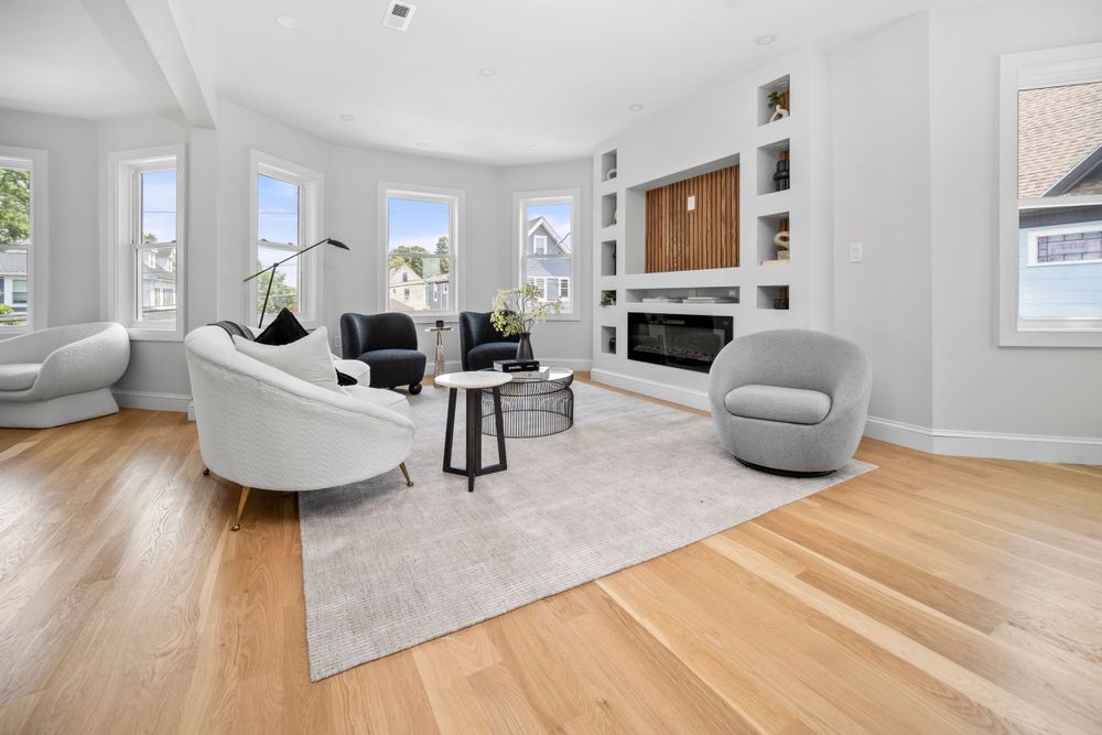 Bright living room with hardwood floors, built-in shelving, fireplace, and large bay windows.