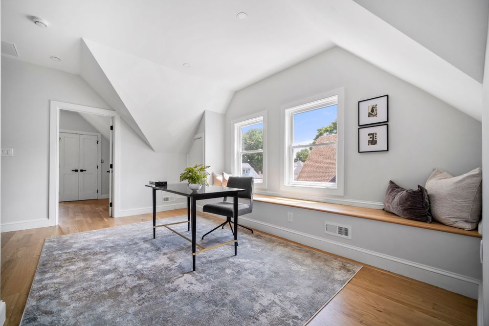 Bright attic home office with vaulted ceilings, built-in window seat, and hardwood floors.