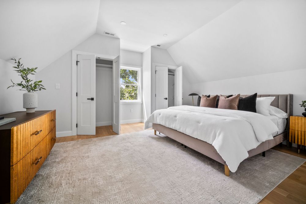 Spacious attic bedroom with vaulted ceilings, large bed, hardwood floors, and dual closets.