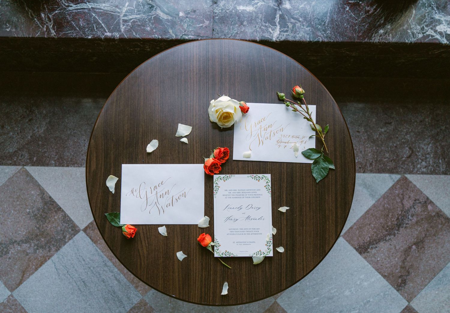 Flat lay detail shot of cream and red floral arrangements beside a hand-calligraphed invitation suite, styled on stone at Nazareth Chapel