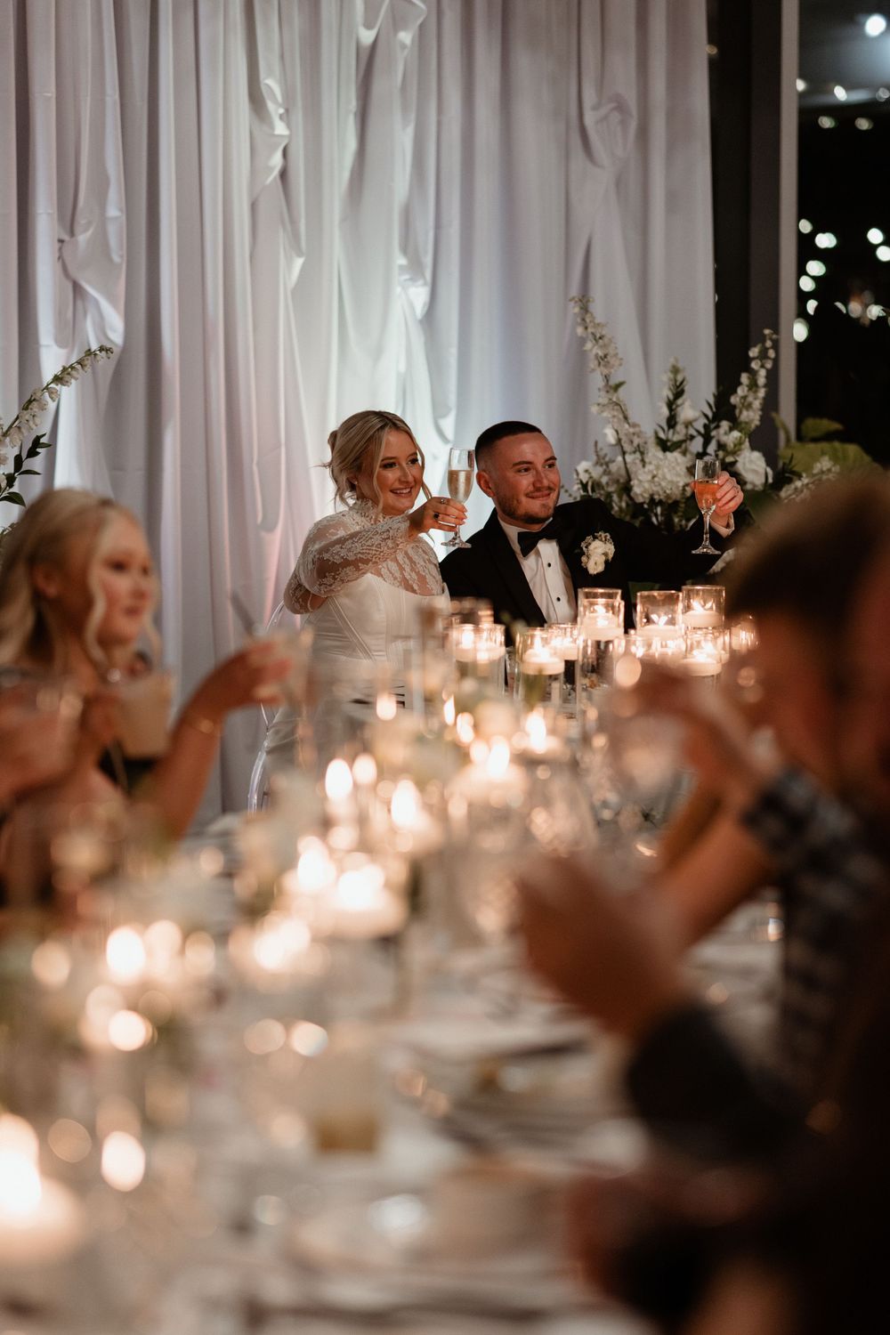 Elegant wedding reception table setting with glowing candles and white drapes creating a romantic atmosphere.