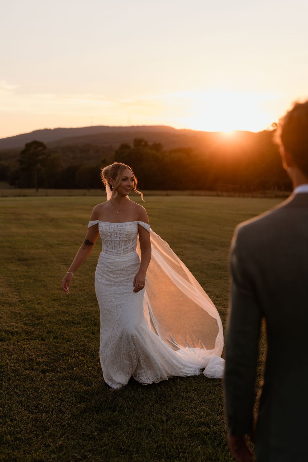 A bride in a white dress twirls in a field at sunset while her veil flows in the golden light.