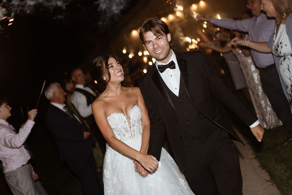 A couple dances together at an evening wedding reception with warm lighting and guests in the background.
