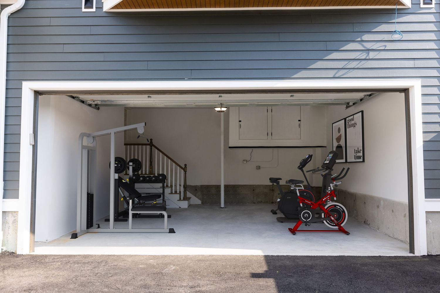 Converted garage home gym featuring exercise bike, weight bench, and fitness equipment on white floors.