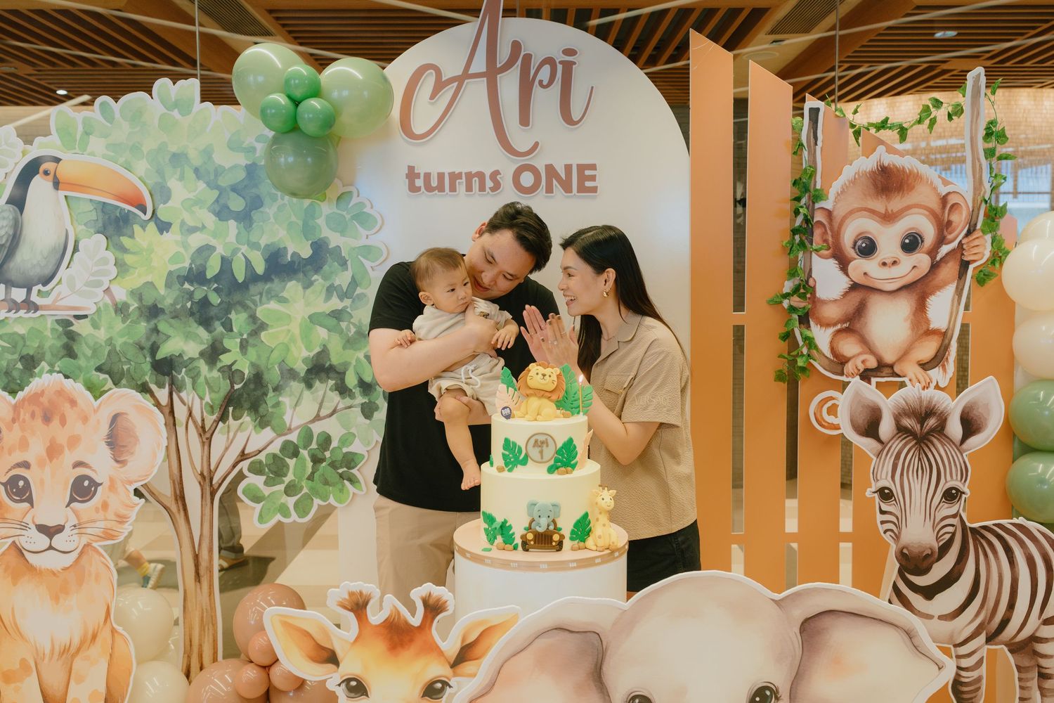 Family celebrates at a baby celebration event with blue and white balloon arch and decorated cake display.