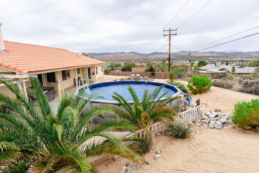 Panoramic desert landscape with palm trees and residential buildings against mountain backdrop and power lines.