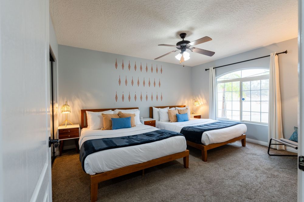Spacious bedroom with wooden bed frame, white bedding, and natural light streaming through windows.