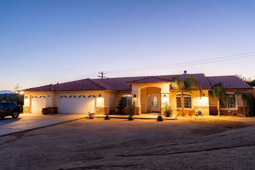A panoramic view of a single-story desert home at dusk with warm lighting glowing from the windows.