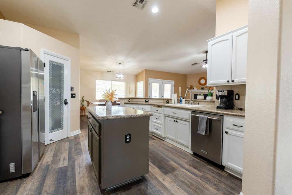 Modern kitchen and living space with gray cabinets, wood-look flooring, and recessed lighting in open concept layout.