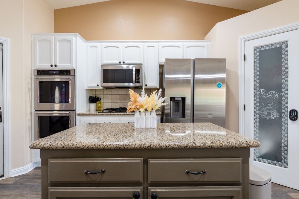 Modern white kitchen with granite countertops, stainless steel appliances, and beige walls in an open concept layout.