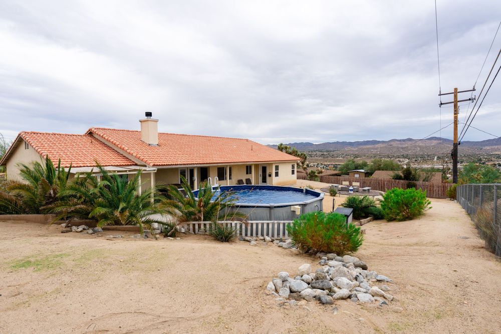 A panoramic view shows multiple residential buildings with red tile roofs against a cloudy desert landscape.