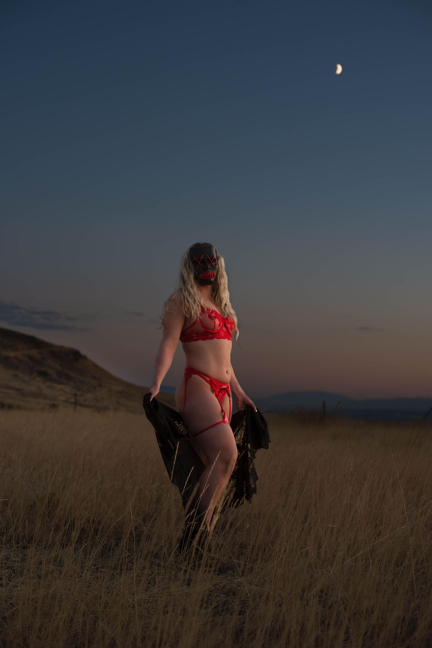 Boudoir photography of a woman in the field at sunset, wearing red lingerie and a mas in Salt Lake
