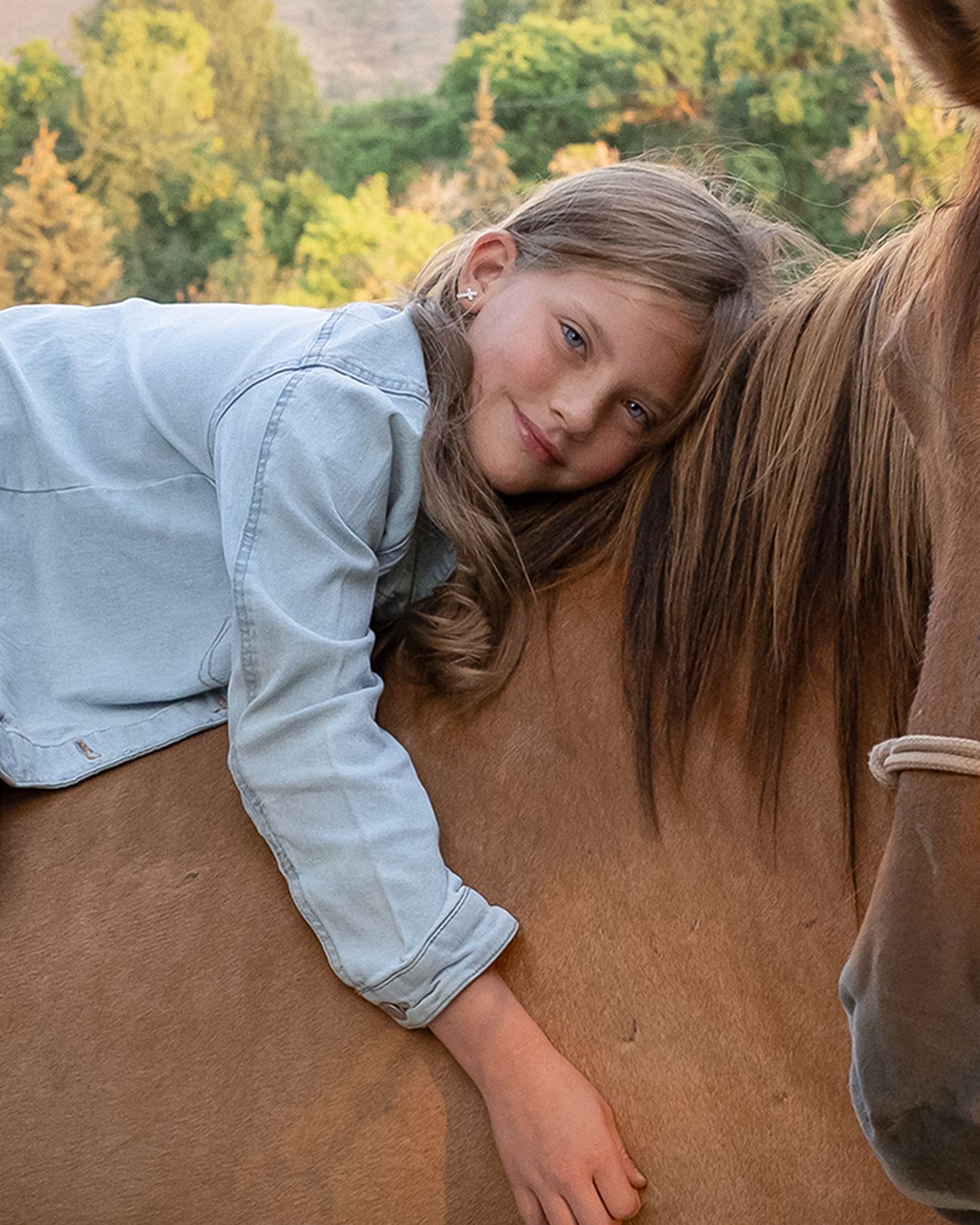 Close-up shot leaning on a brown horse's back in casual denim attire.