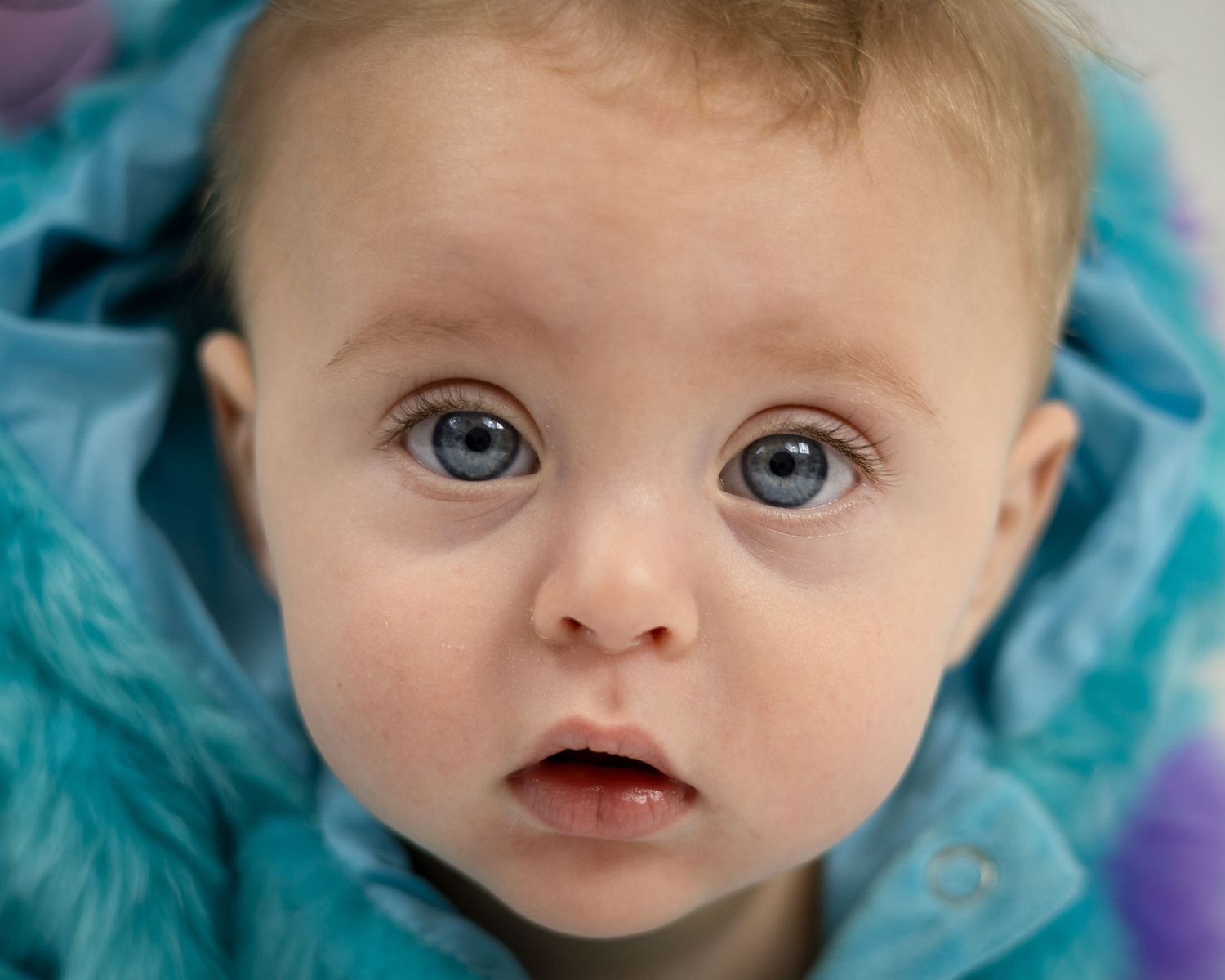 Close up portrait of a baby with bright blue eyes wearing a turquoise outfit.