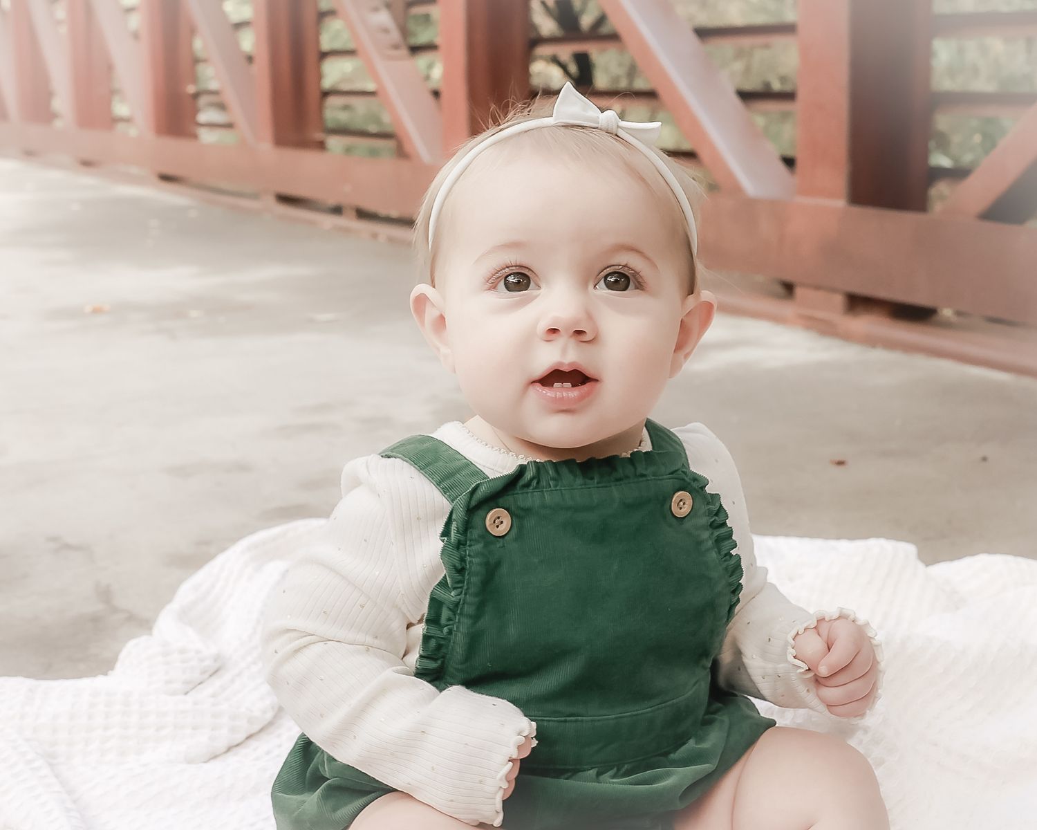 Baby wearing a dark green romper with white sleeves sits on a light colored surface.