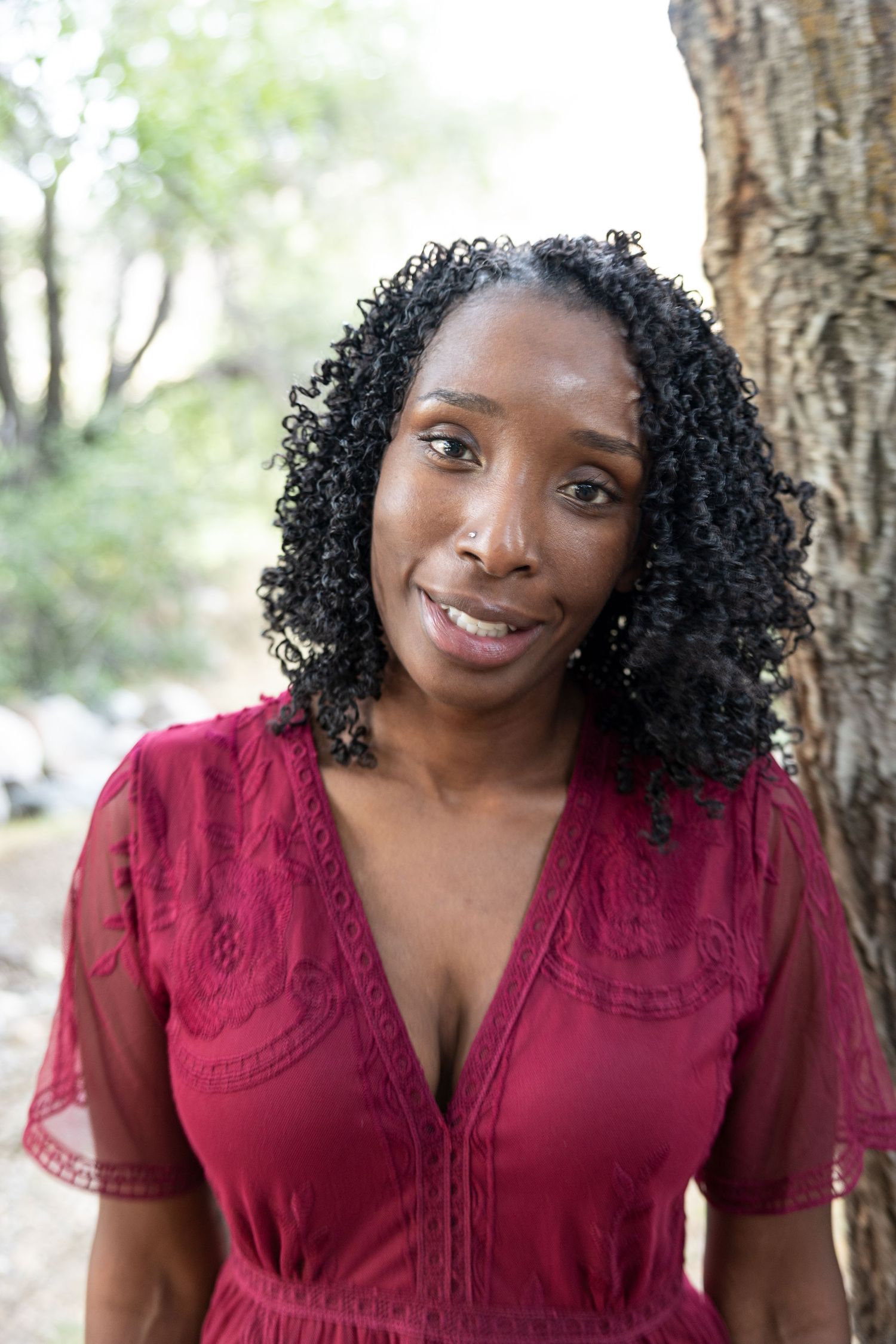 A series of four photos showing a person in a burgundy lace top smiling outdoors against a natural background.