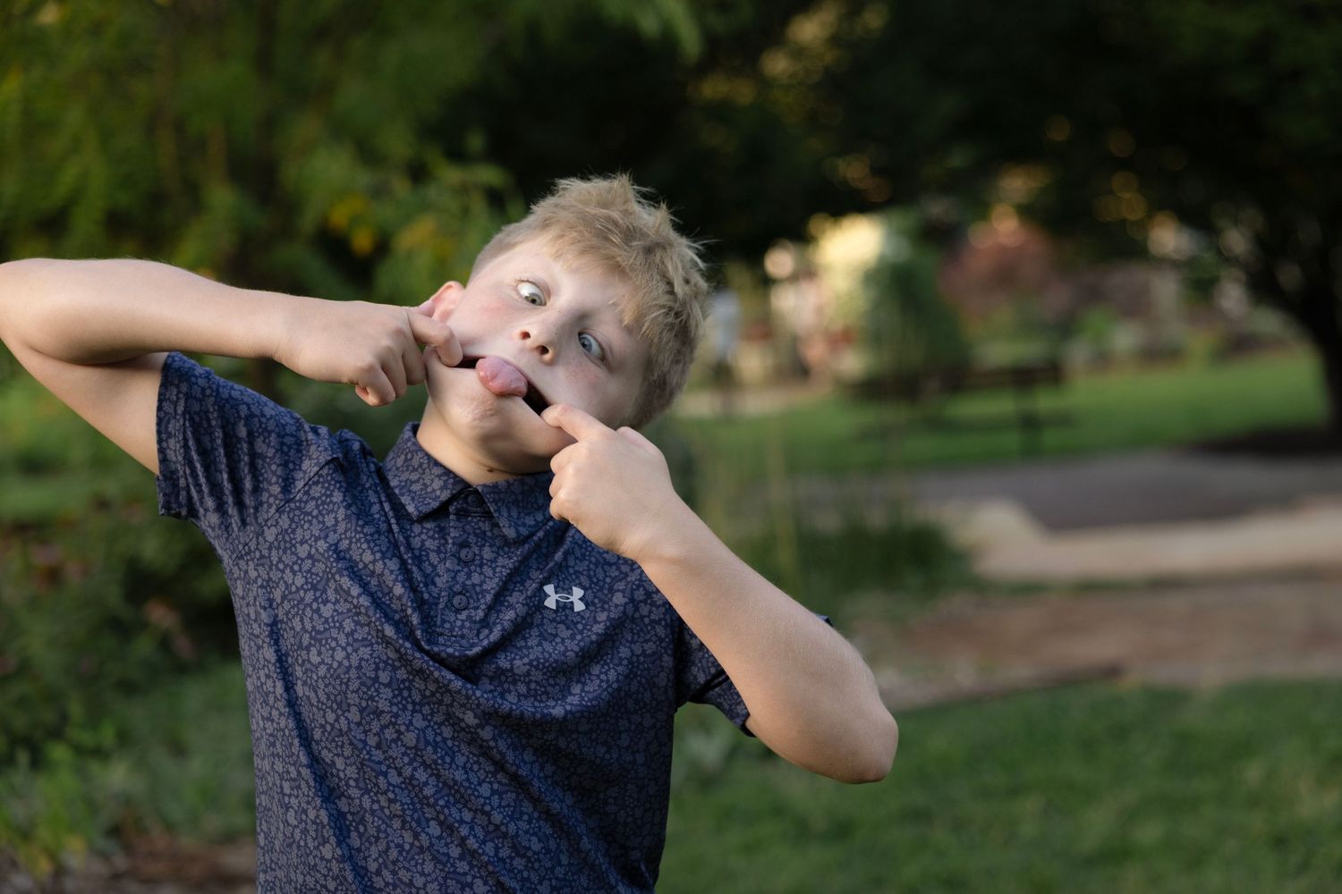 A person in a navy blue t-shirt stands outdoors in a grassy area while looking up at the sky.