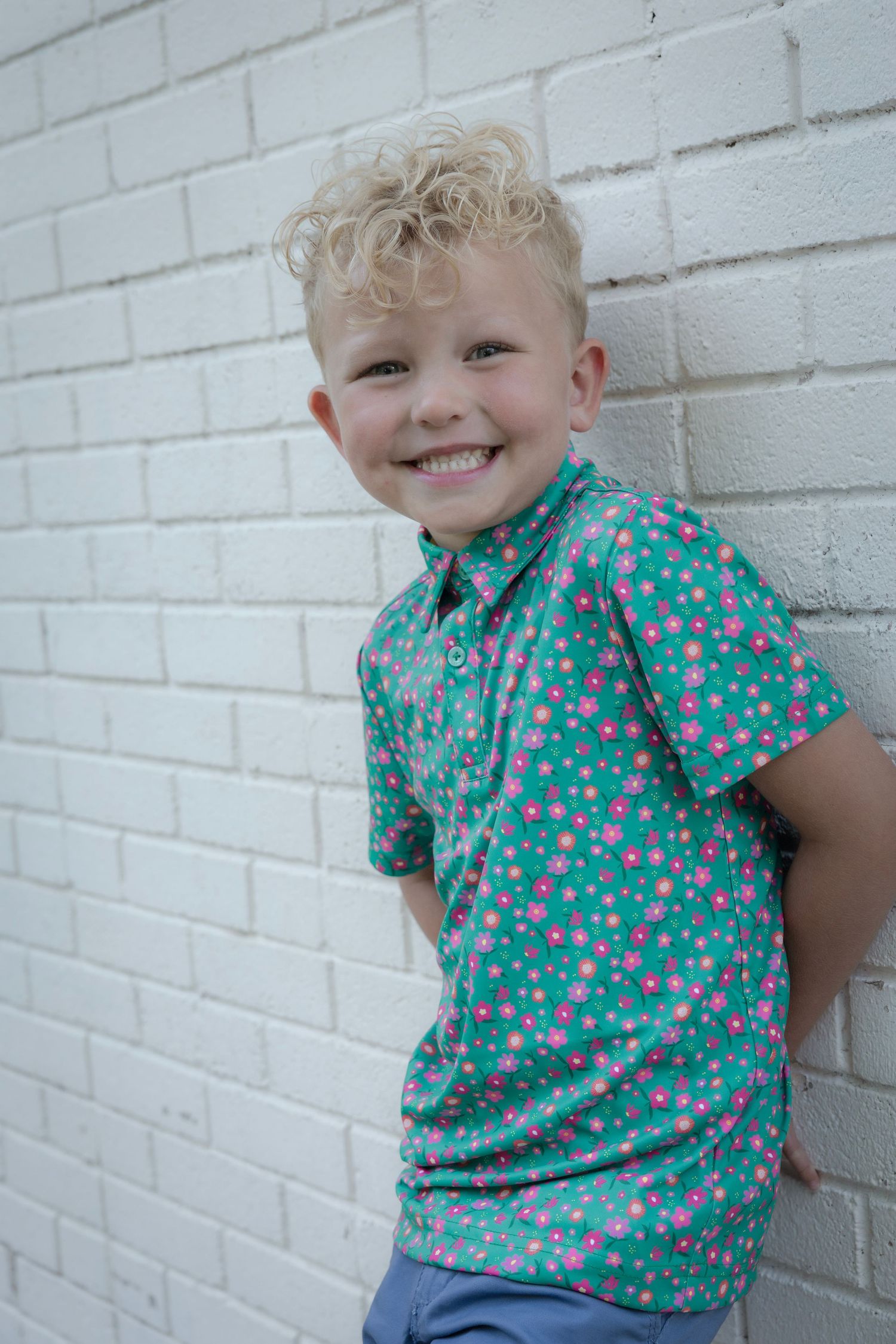 A child in a turquoise polka dot shirt poses playfully against a white brick wall in a series of candid shots.