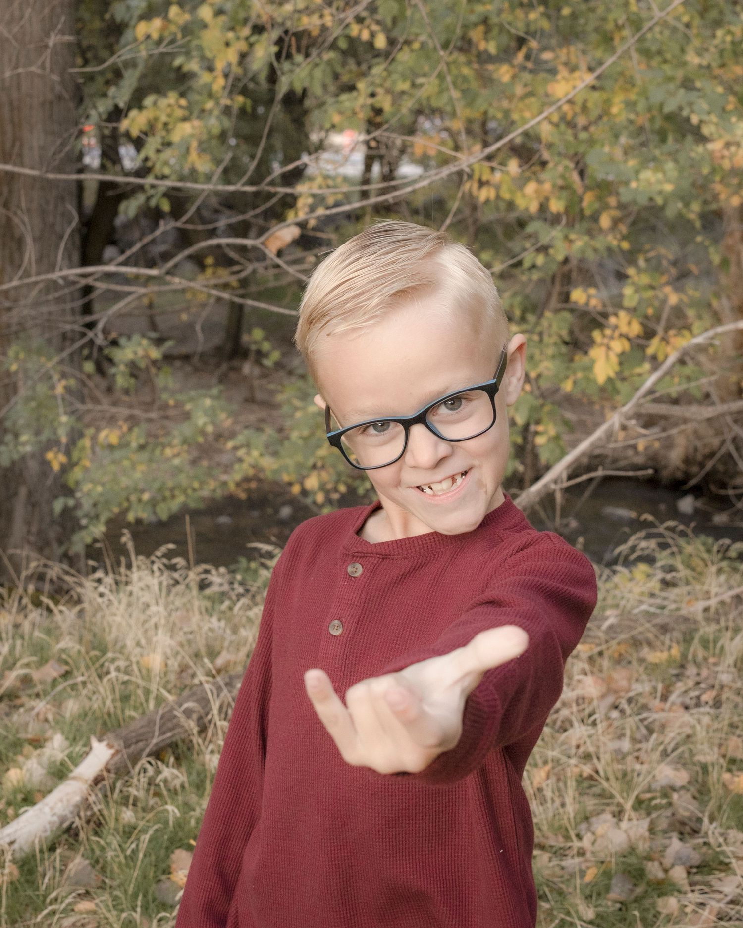 A person wearing glasses and a burgundy sweater makes playful gestures in a series of outdoor portrait shots.