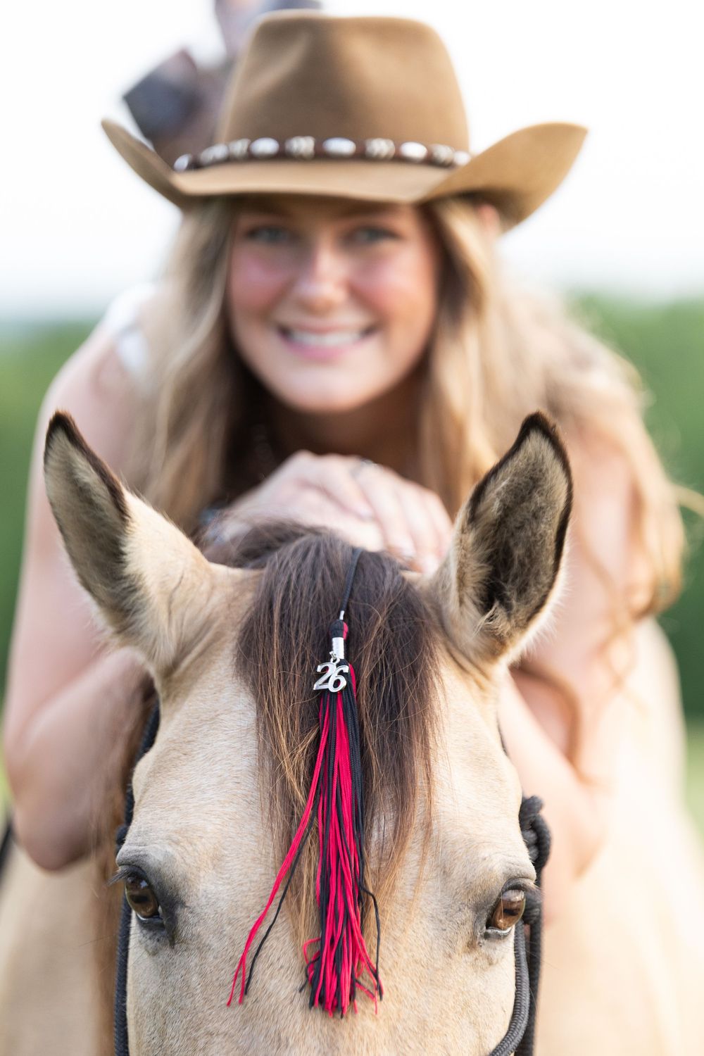 girl laying over horse's neck, camera focused on the horse's face with graduation tassel in the horse's forelock
