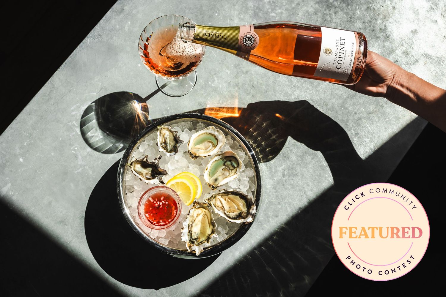 Fresh oysters on ice with lemon and cocktail sauce, paired with a glass of rosé wine being poured from a bottle.