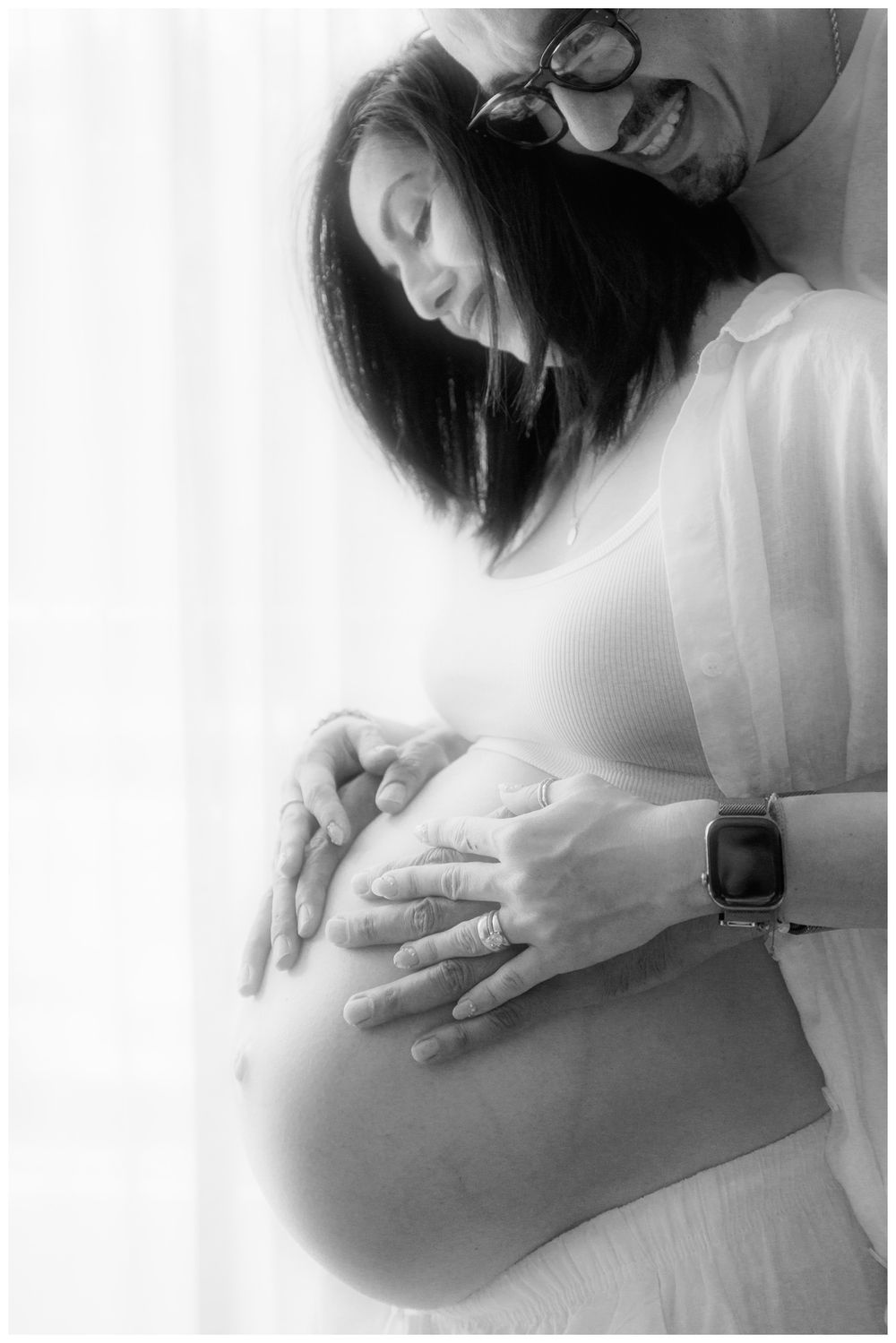 Black and white maternity photo of couple tenderly cradling pregnant belly, soft natural light, intimate moment.