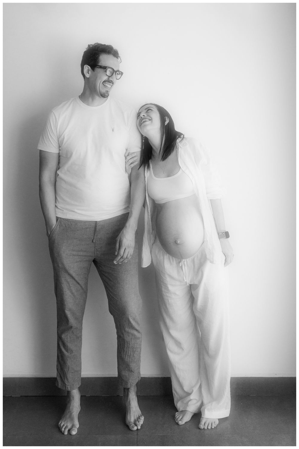 Black and white maternity photo of a laughing couple standing together, the woman showing her pregnant belly.