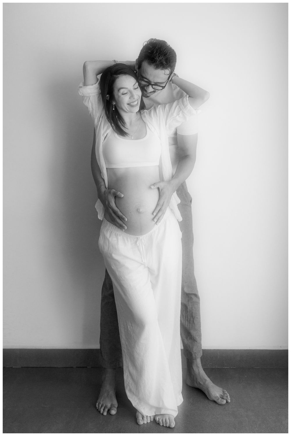 Black and white maternity photo of couple embracing, man kissing womans head while holding her baby bump.