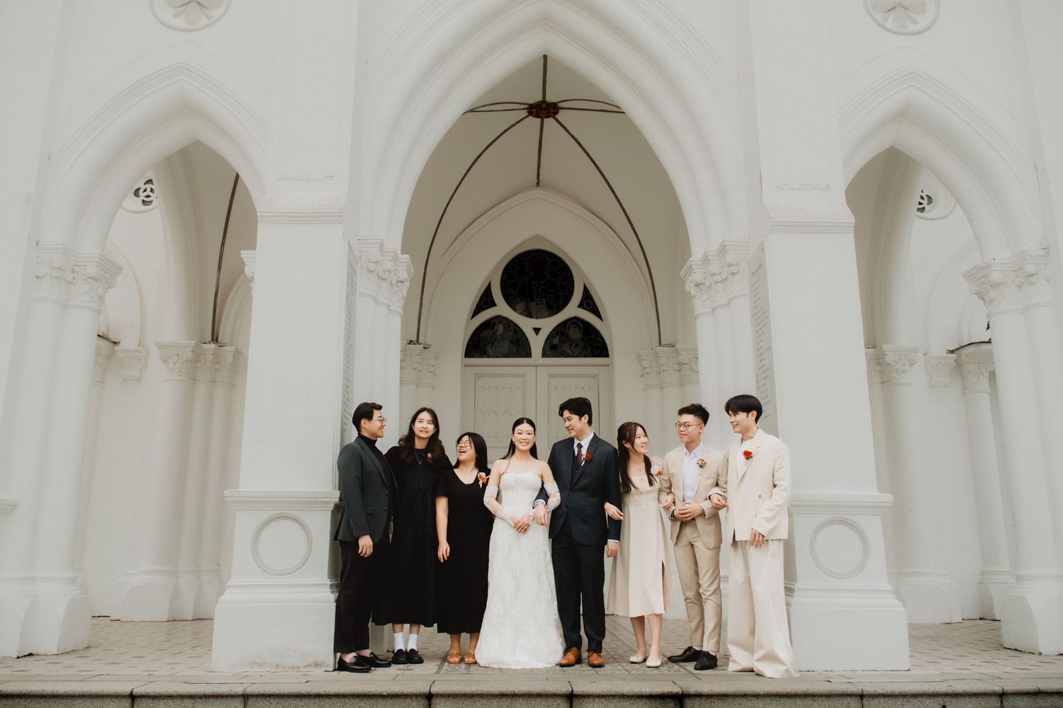 Wedding party poses under gothic arches of white church architecture. Singapore