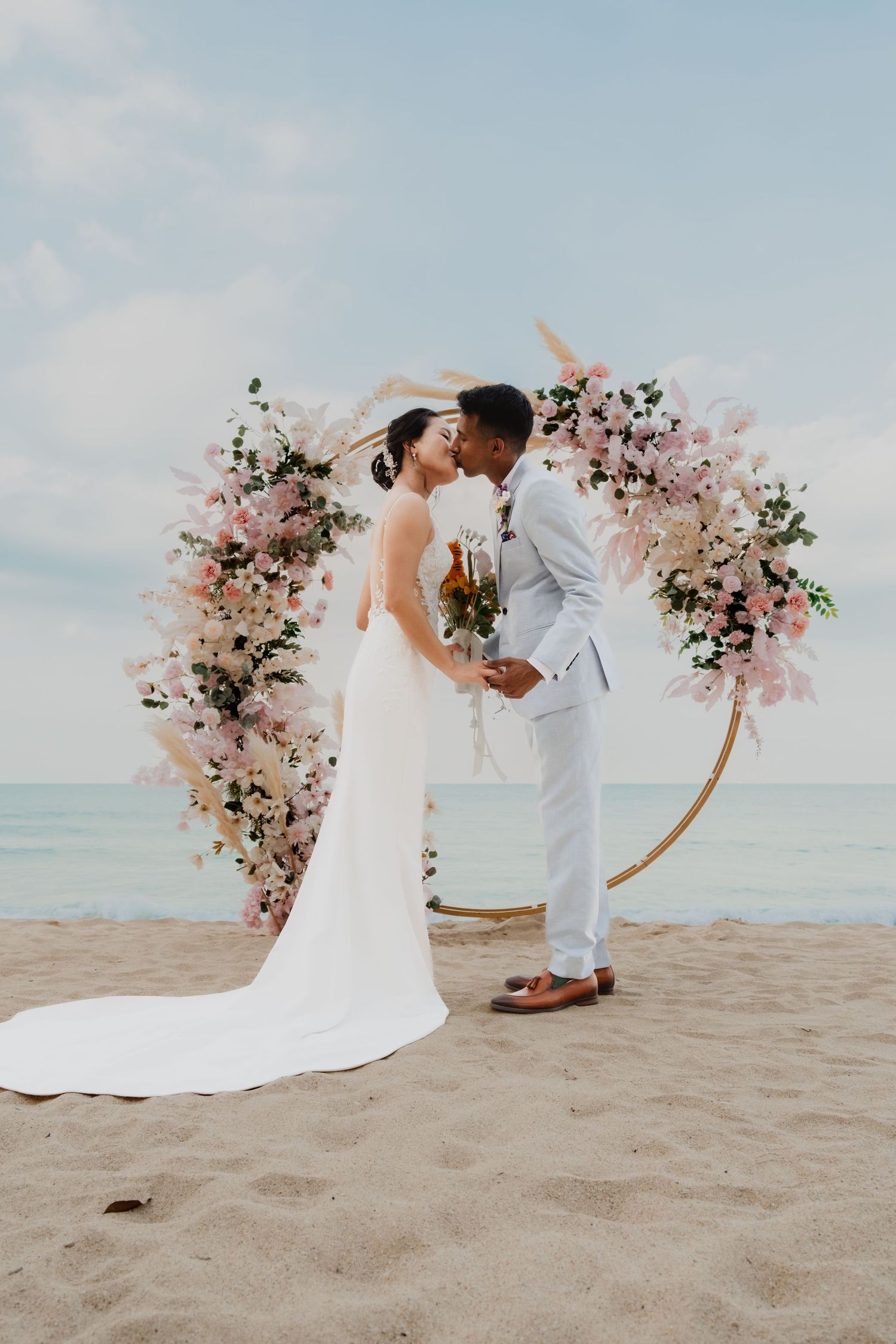 A romantic beach wedding ceremony setup with a floral arch and couple sharing a moment on the sand. Singapore
