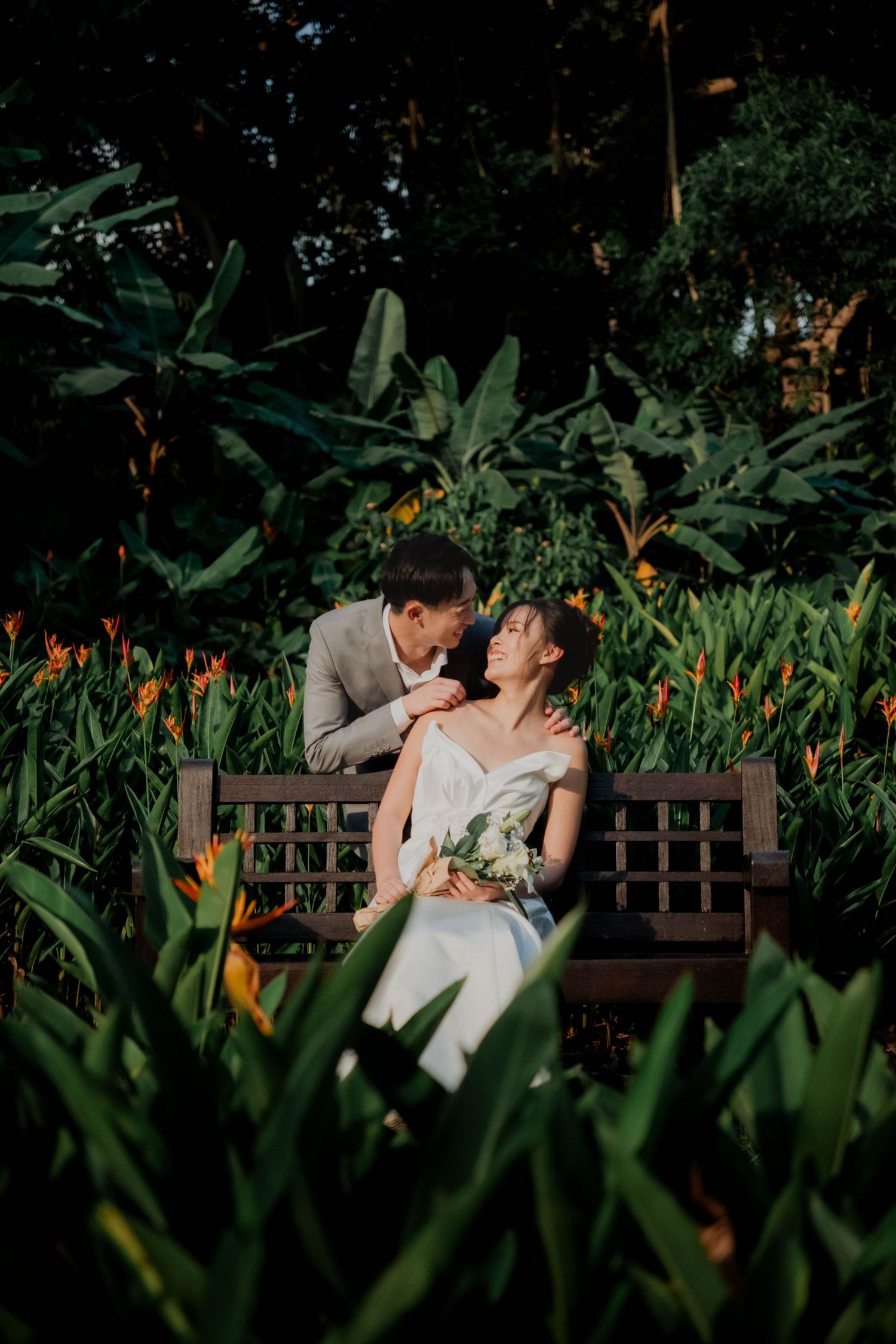 Romantic garden photoshoot with couple on wooden bench surrounded by tropical plants and flowers. Singapore