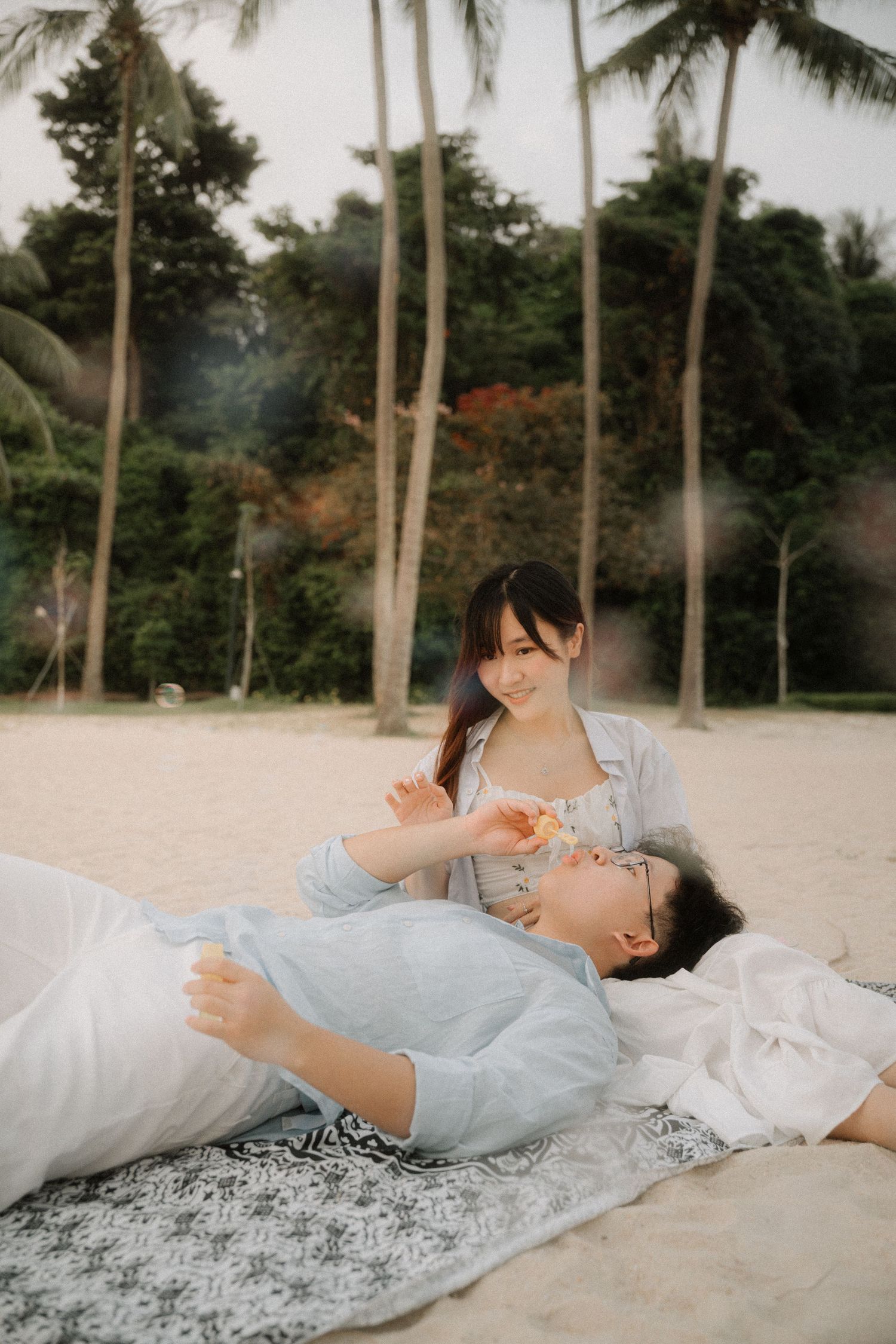 Couple sharing tender moments on a blanket under palm trees on a tropical beach. Singapore
