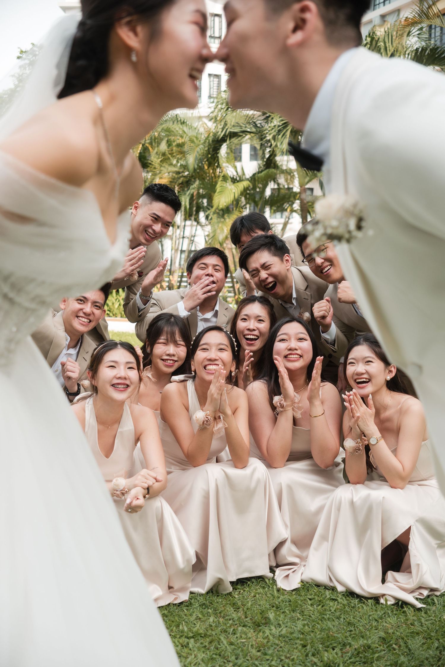 Fun Photoshoot of Wedding bridal party in light pink dresses laughs together while sitting on grass during outdoor celebration.