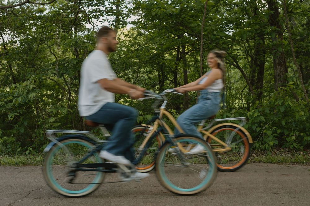 Couple riding colorful cruiser bikes together on a path surrounded by lush green trees.