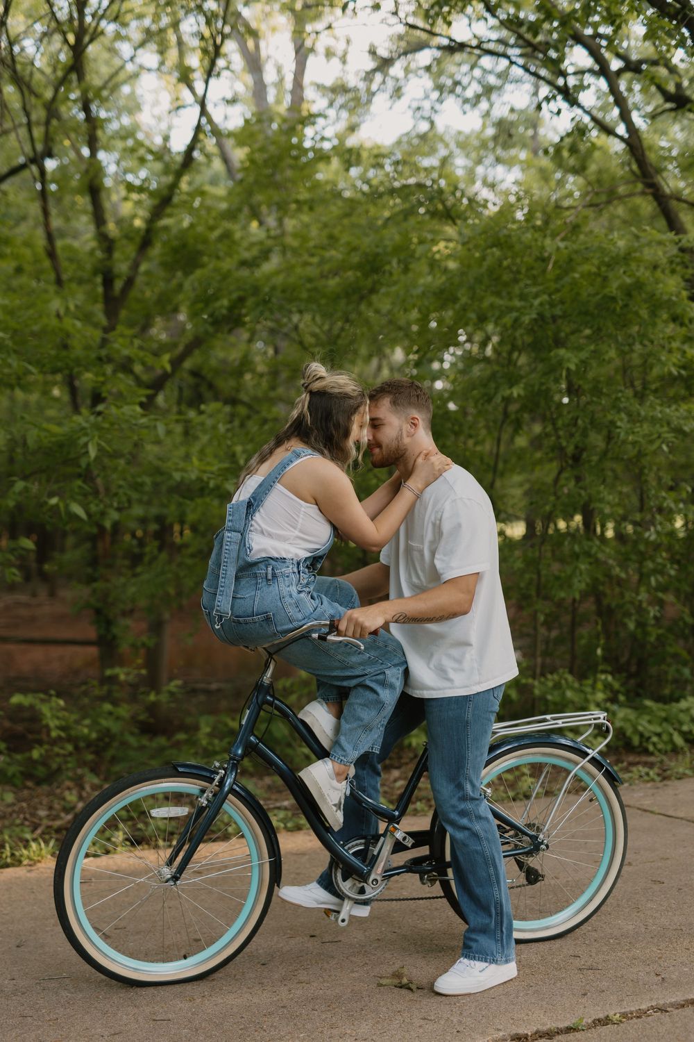 Romantic couple sharing an intimate moment on a vintage teal bicycle in a lush green park.